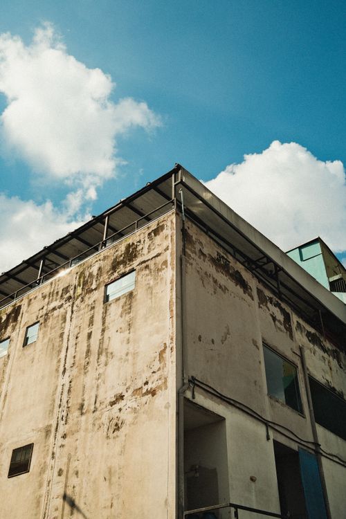 Free Corner of aged building with peeling facade under a bright blue sky with clouds. Stock Photo