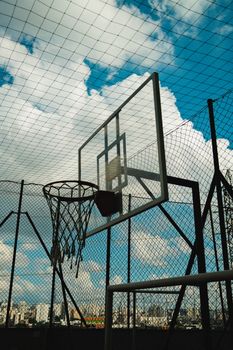 Outdoor basketball court with net and hoop against a vibrant blue sky with clouds.