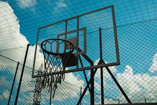 A minimalist view of a basketball hoop outdoors with a clear blue sky and clouds in the background.