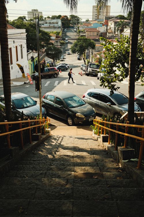 Free A bustling urban street scene captured from a stone staircase, highlighting parked cars and pedestrians. Stock Photo