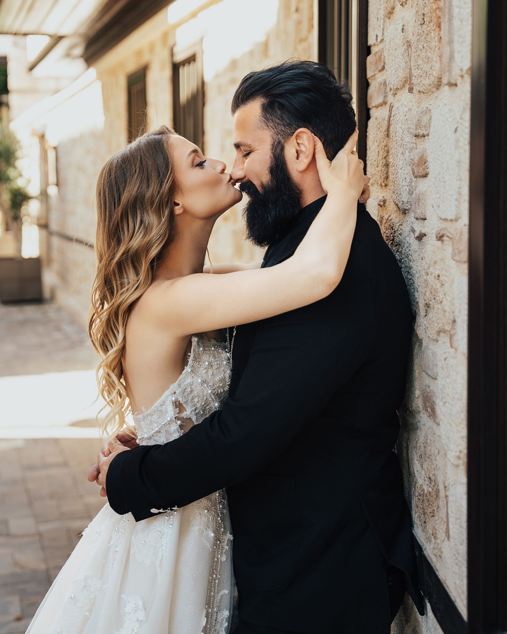 A romantic moment between a bride and groom embracing outside against a rustic wall.