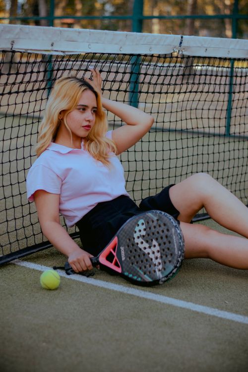 Free Young woman sitting on a tennis court, holding a racket beside the net, with a casual pose. Stock Photo