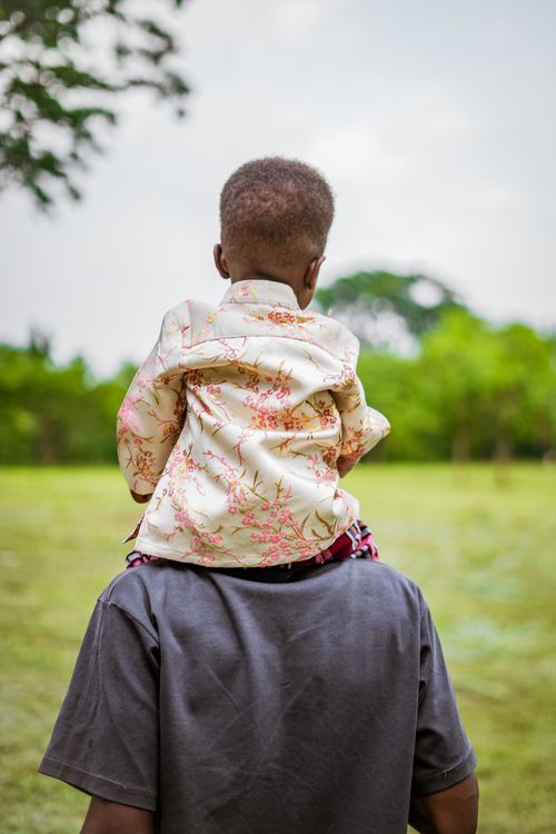 Free Rear view of a child on their father's shoulders in a green park setting, embracing nature. Stock Photo