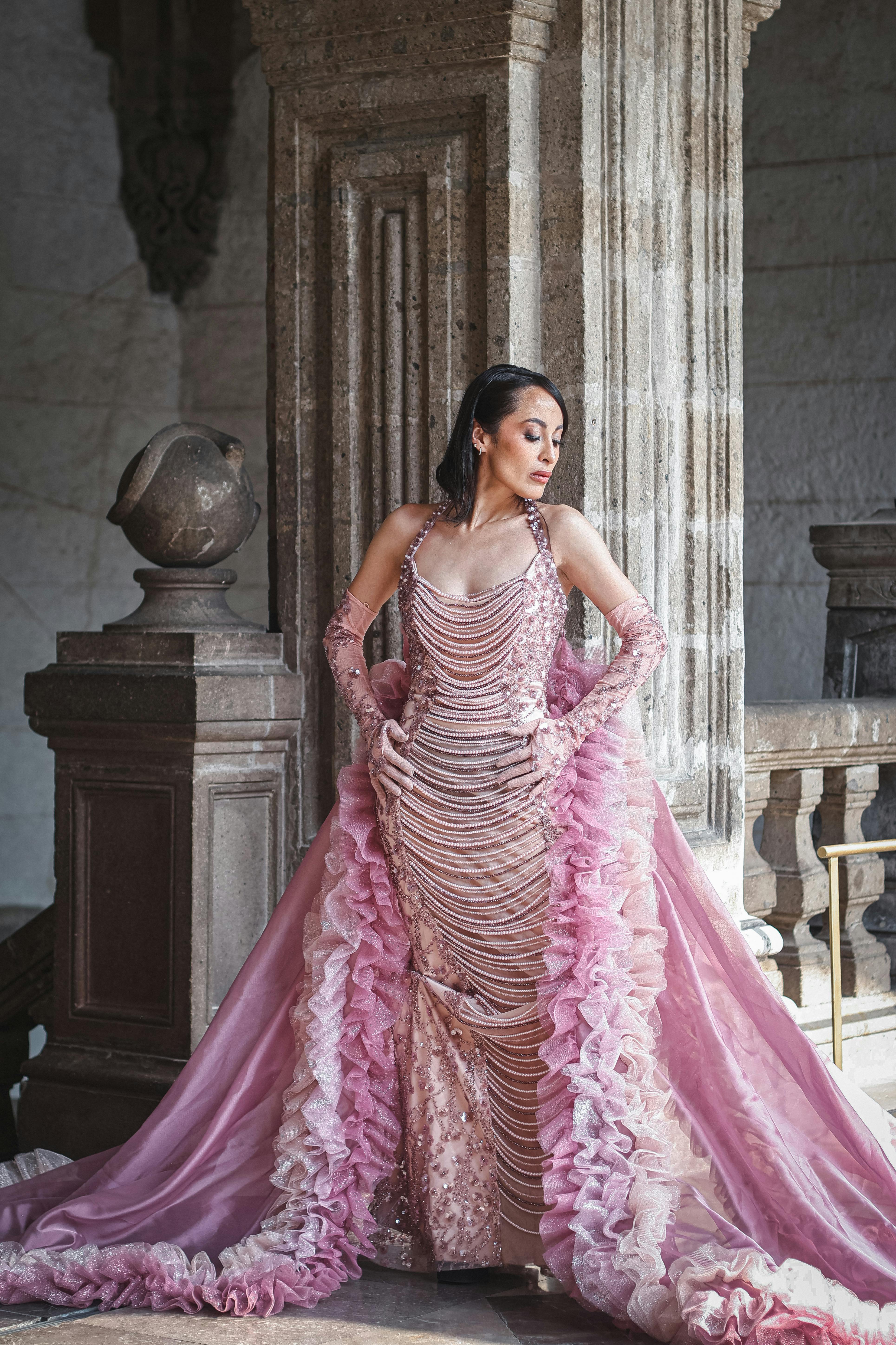 gratis Een vrouw in een prachtige roze jurk poseert elegant op een historische locatie. Stockfoto