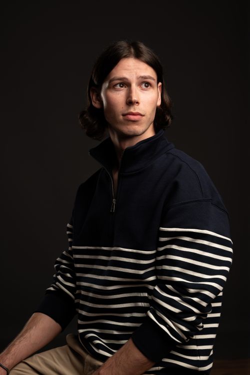 Free Portrait of a young adult male in a striped sweater against a dark backdrop. Stock Photo