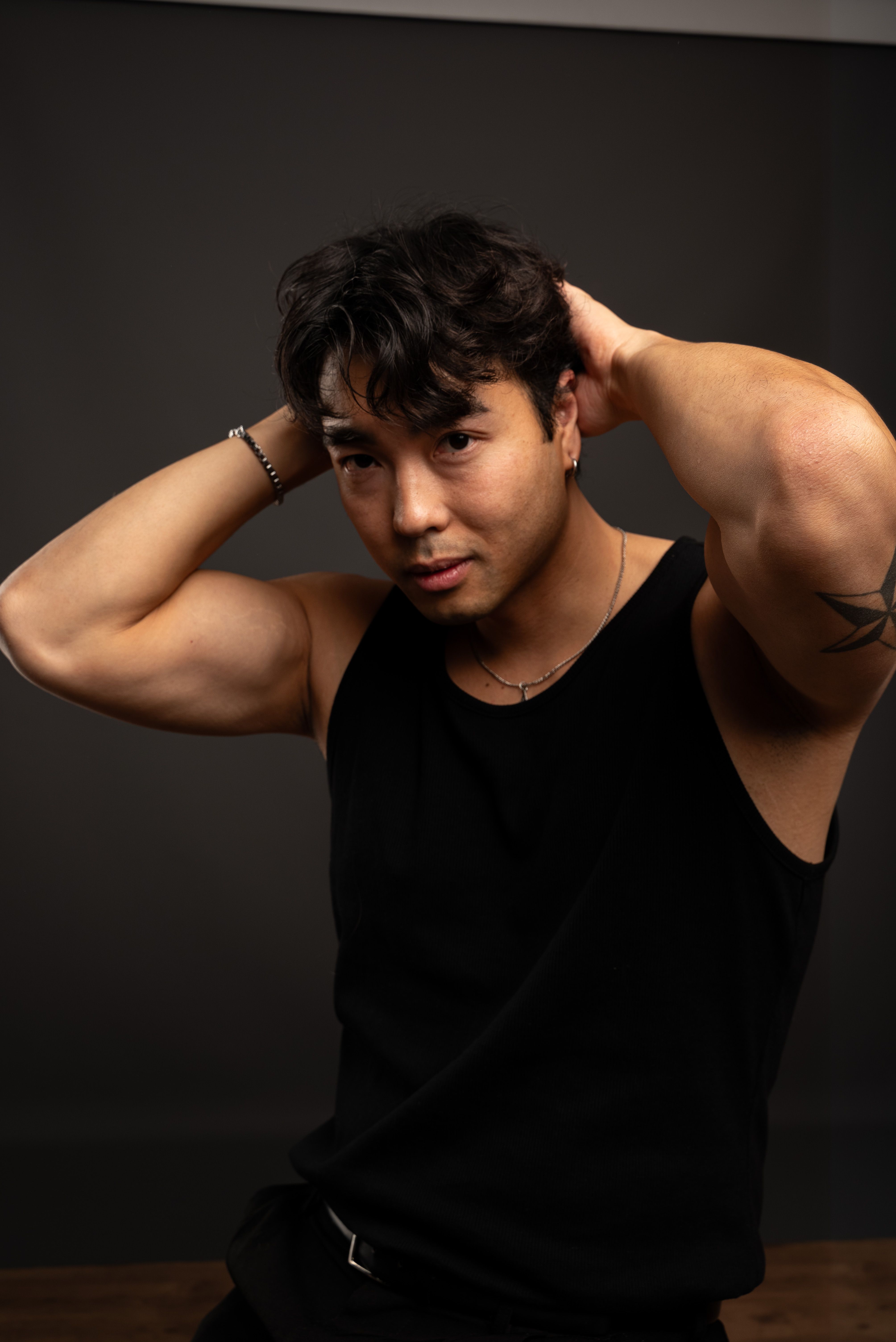 Strong and confident Asian man posing with hands on head against dark background.