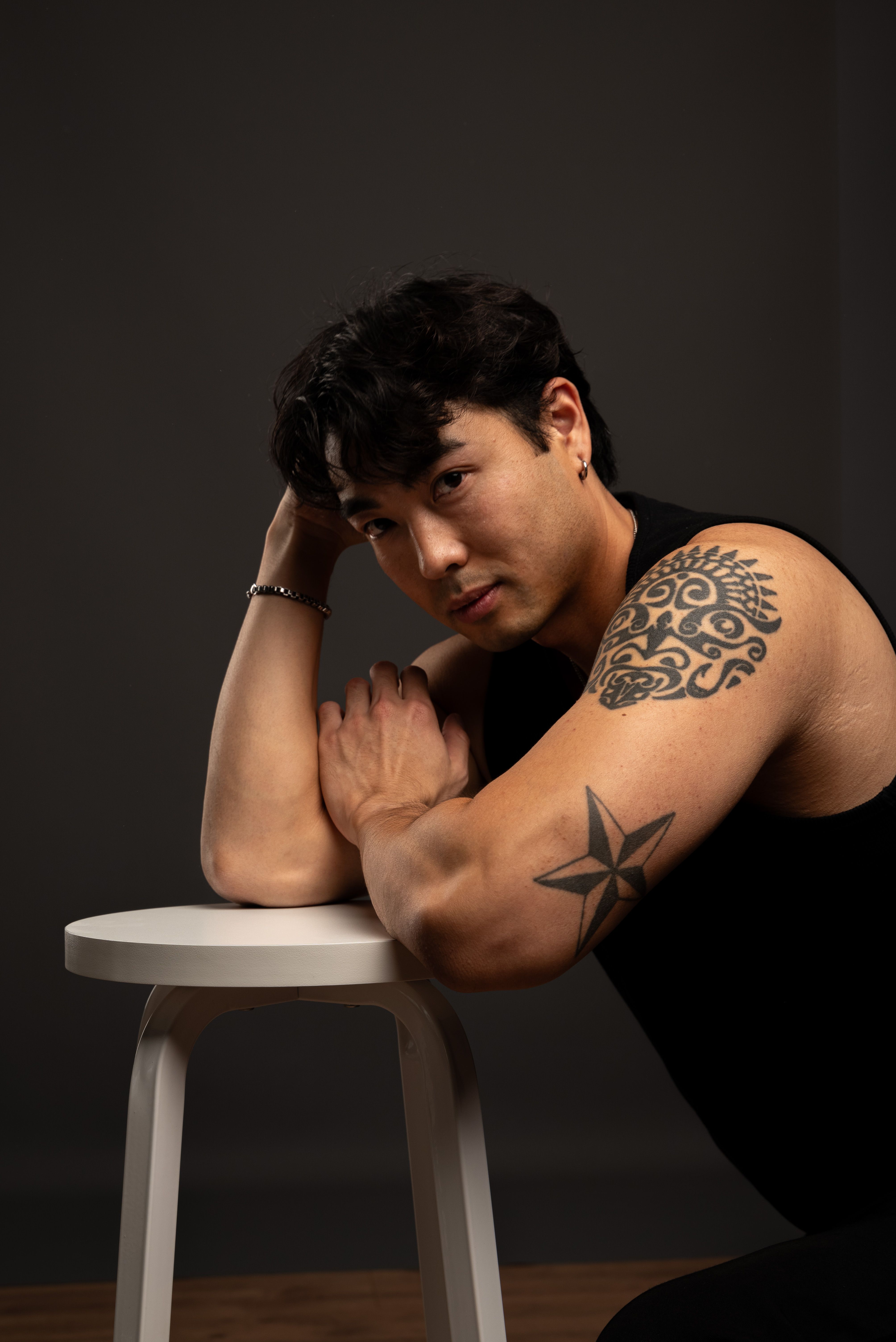 Portrait of a tattooed man posing confidently on a stool indoors.