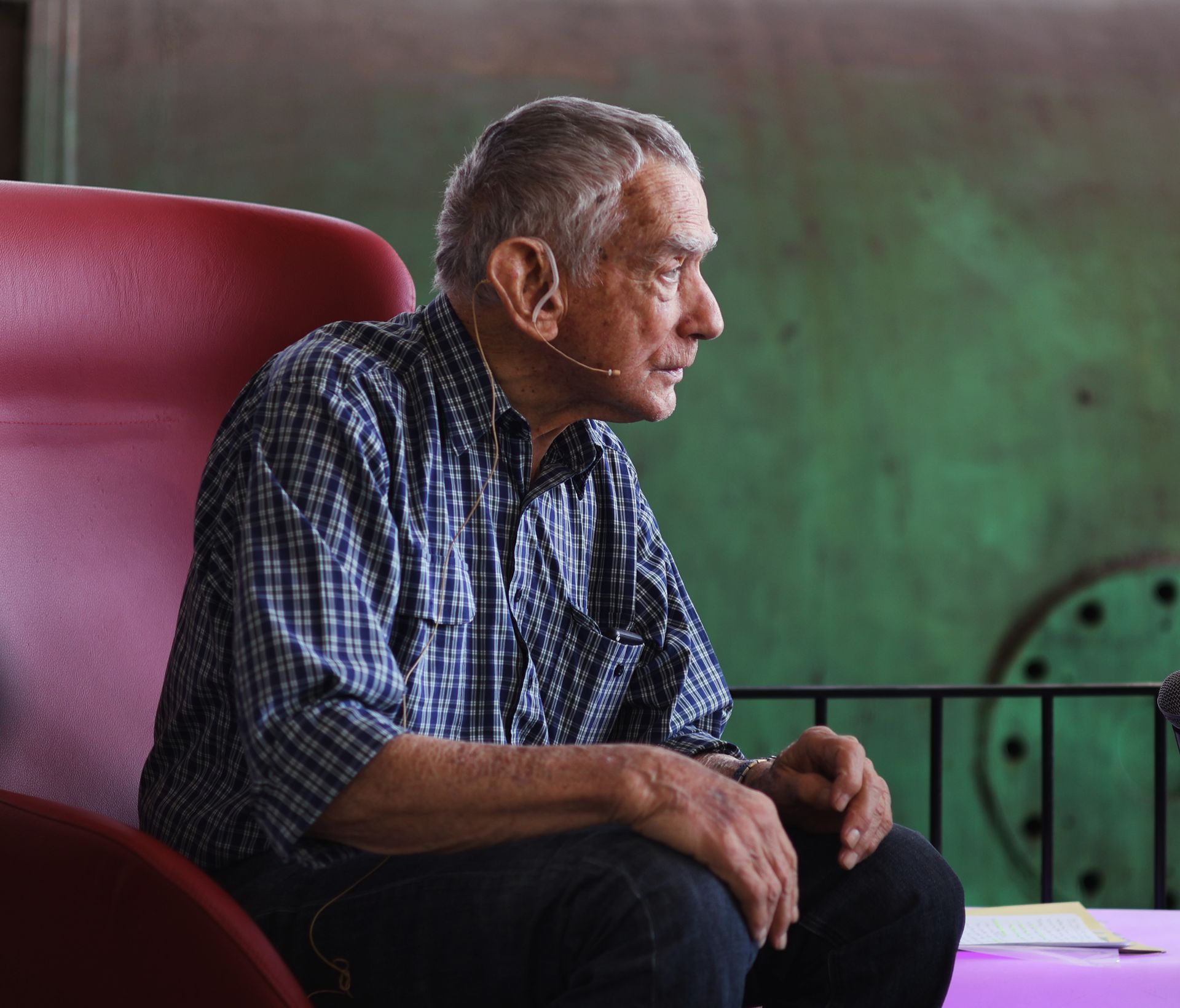 Profile of senior man with microphone speaking indoors.
