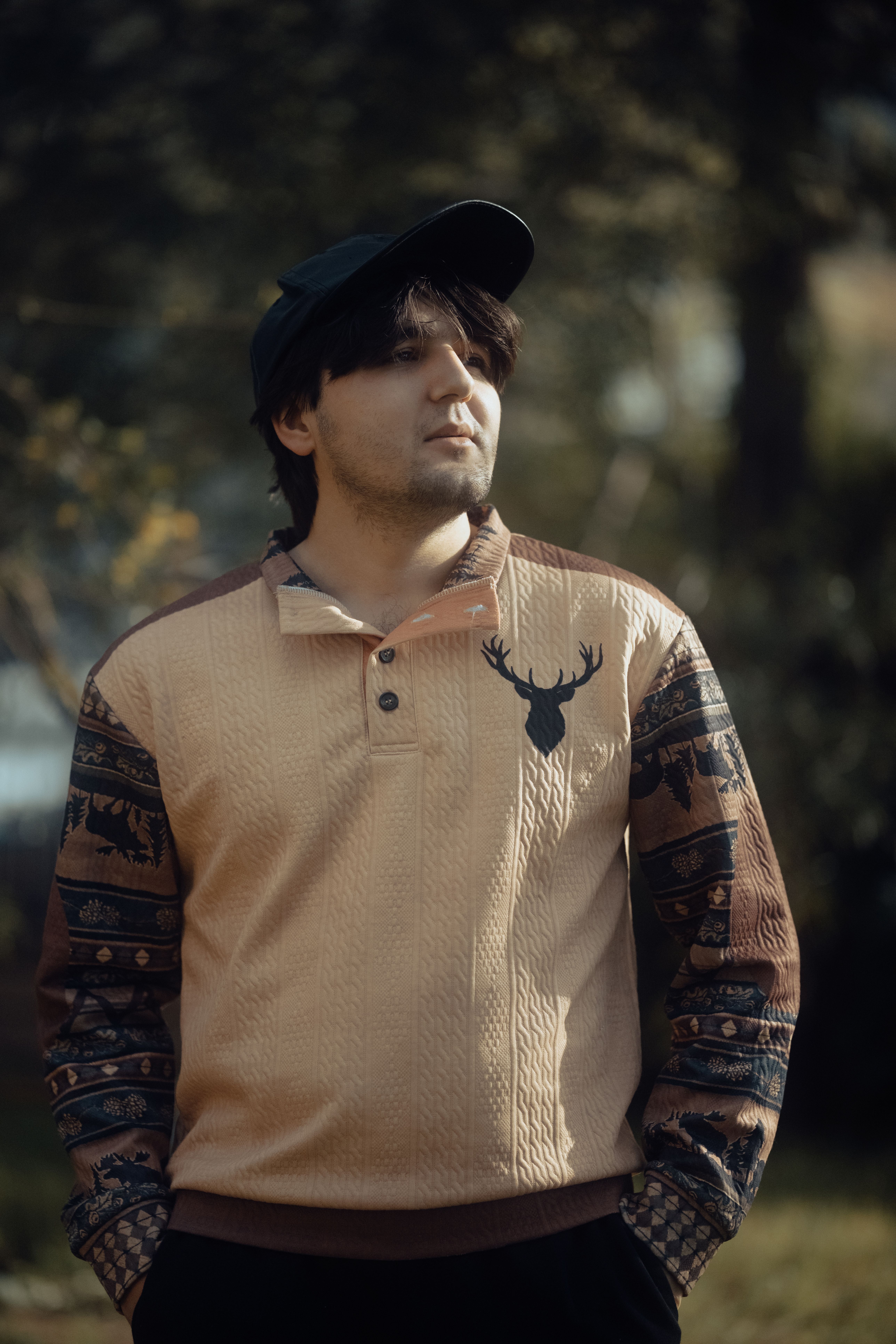 Young man outdoors wearing a fashionable sweater with deer design, enjoying nature.