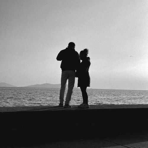 Free Black and white silhouette of a couple standing together by the ocean shore. Stock Photo