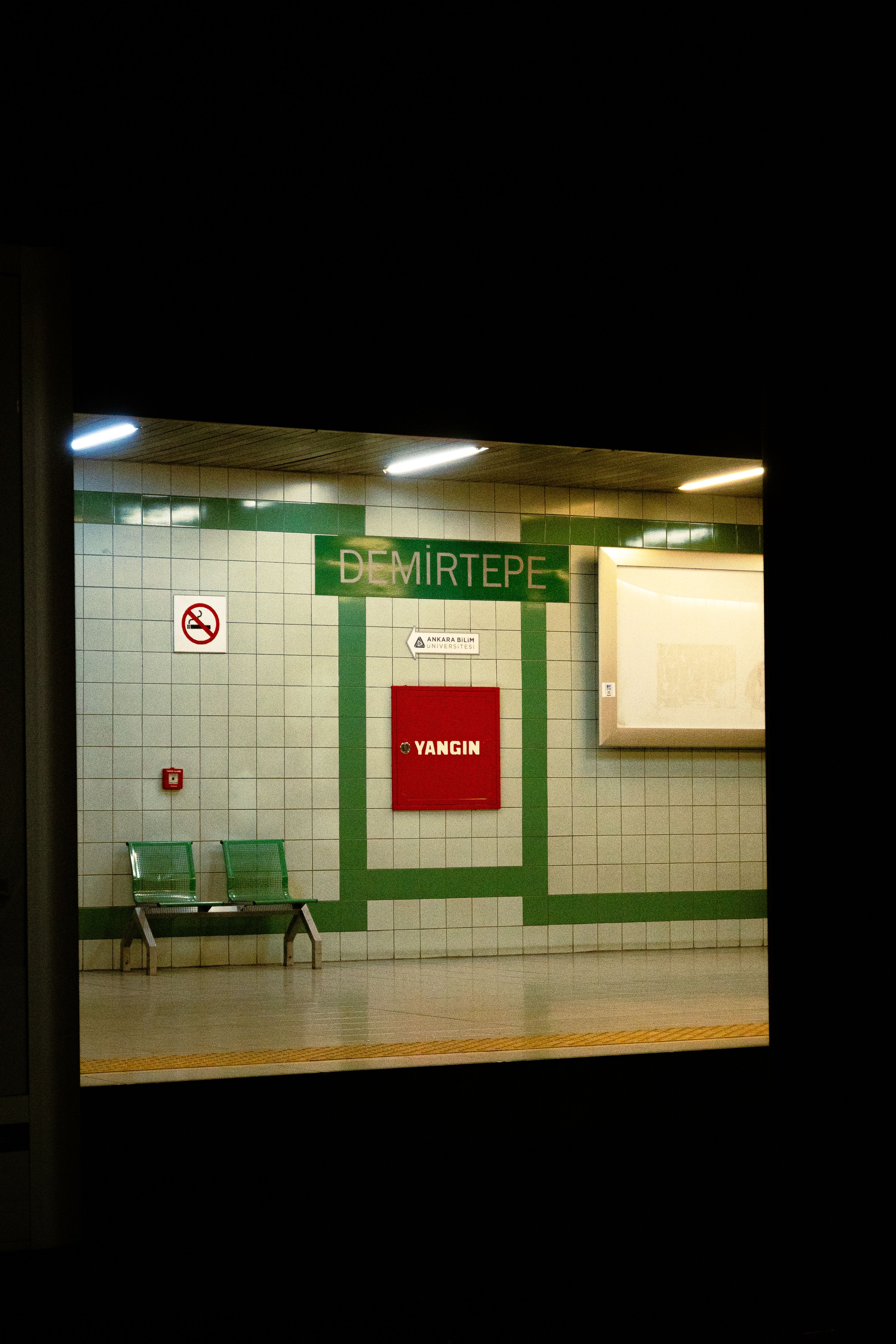 Dimly lit Demirtepe subway platform with empty seats and signage.