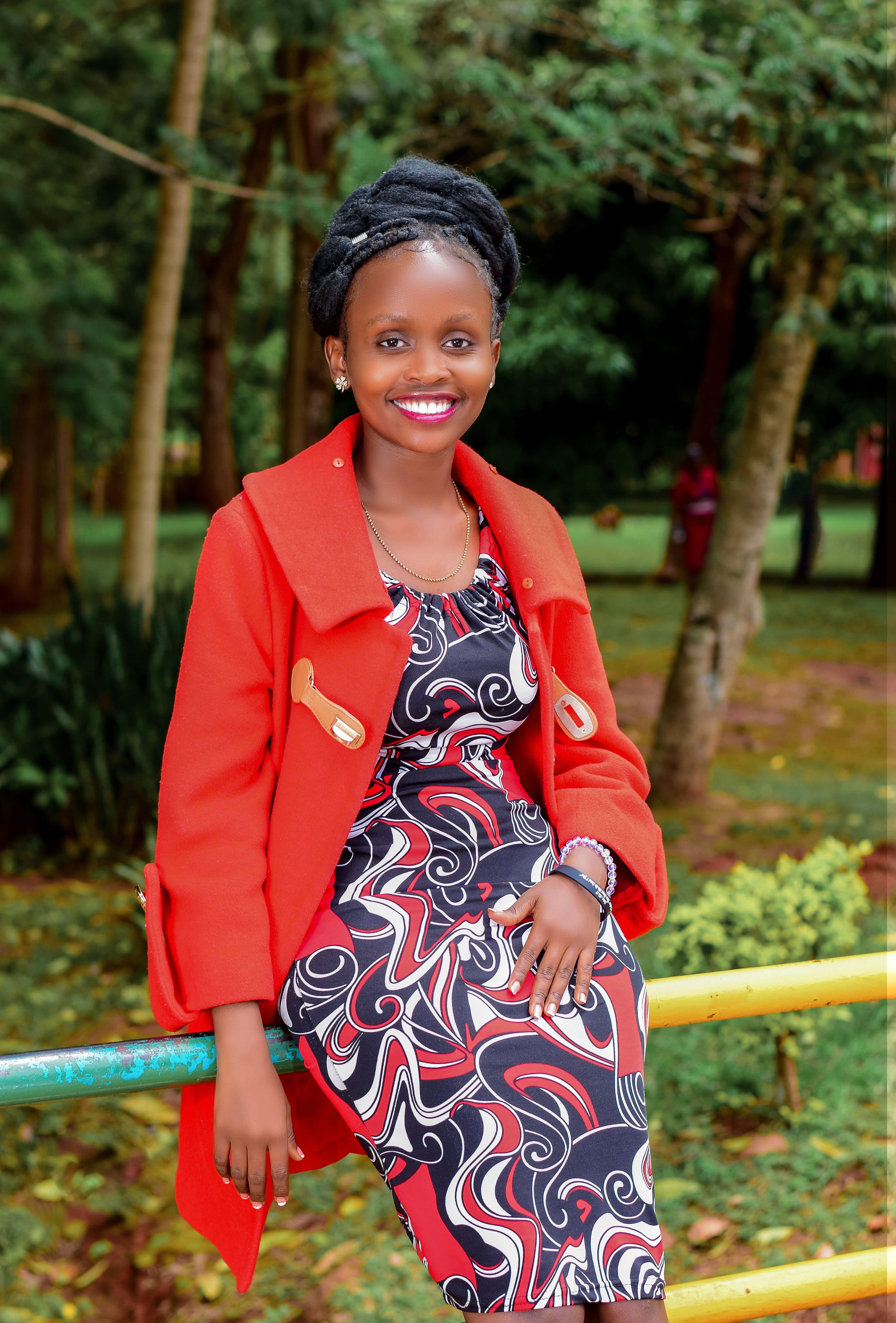 Stylish African woman in vibrant outfit posing confidently in a lush outdoor setting.