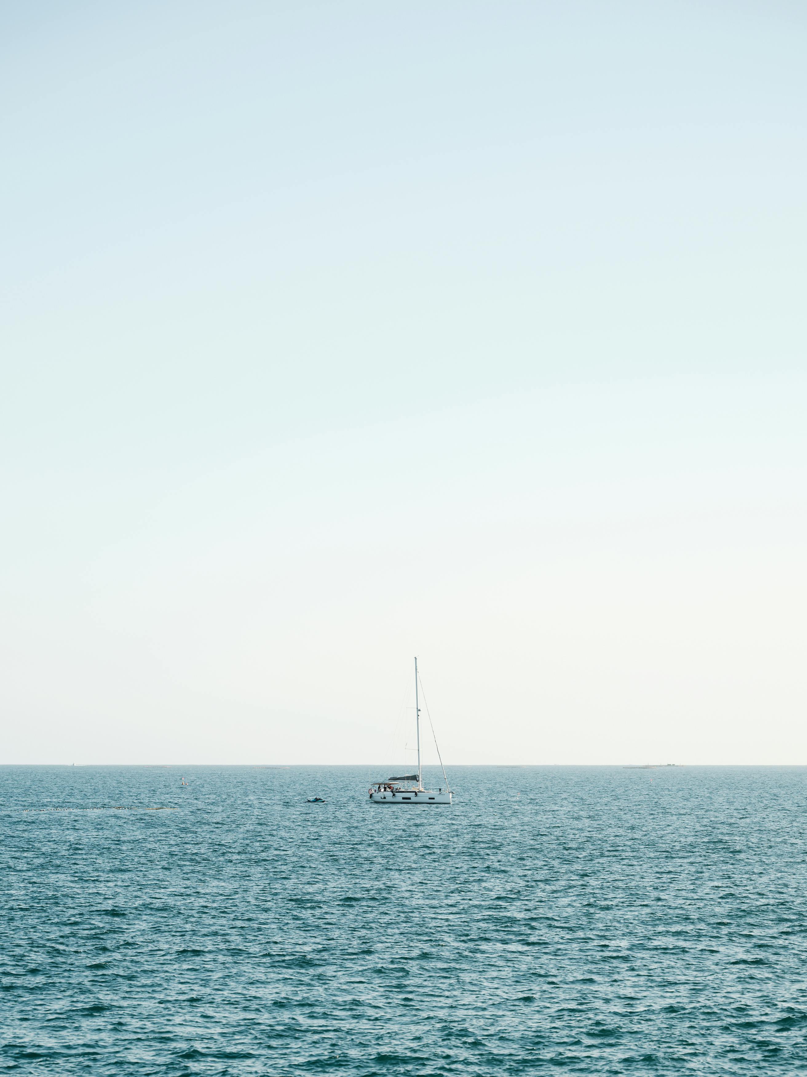 A tranquil scene of a yacht sailing on the calm blue ocean under a clear sky.