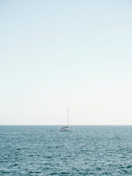 A tranquil scene of a yacht sailing on the calm blue ocean under a clear sky.