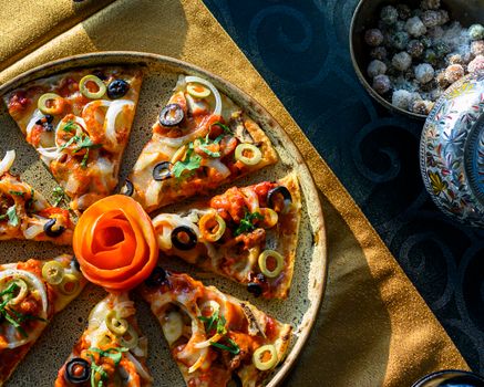 Top view of a vibrant Italian pizza with olives, onions, and a rose garnish, set on a golden tablecloth.