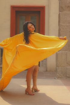 Woman in vibrant yellow dress posing elegantly in an outdoor setting.