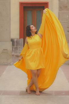 Woman in a flowing yellow dress poses indoors with elegance and style.