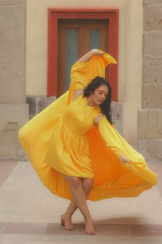 Woman in flowing yellow dress gracefully dancing against stone backdrop.