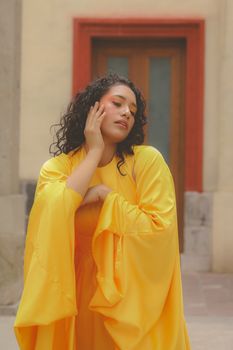 Stylish woman in a bright yellow dress posing gracefully outdoors.