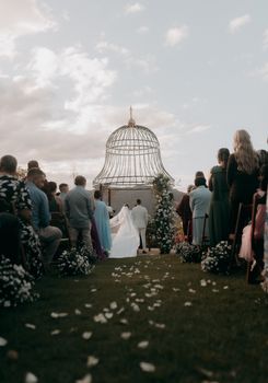 Beautiful outdoor wedding ceremony with guests under decorative gazebo.