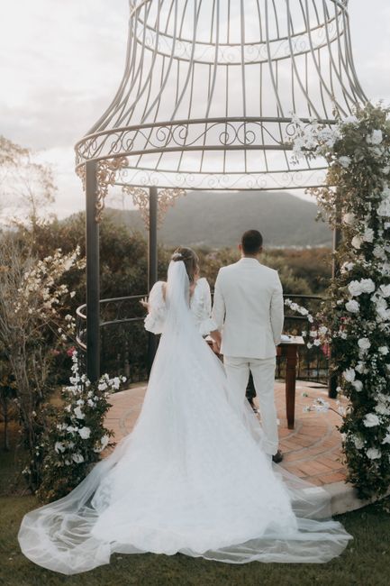 A couple standing under a floral gazebo during their wedding ceremony with scenic mountain backdrop.