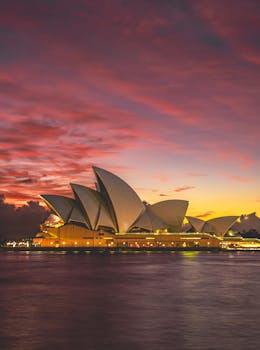 Stunning view of the Sydney Opera House against a vibrant sunset sky, reflecting on the harbor waters.