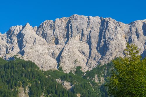 Free A breathtaking view of rugged Alpine mountains with lush greenery and a clear blue sky. Stock Photo