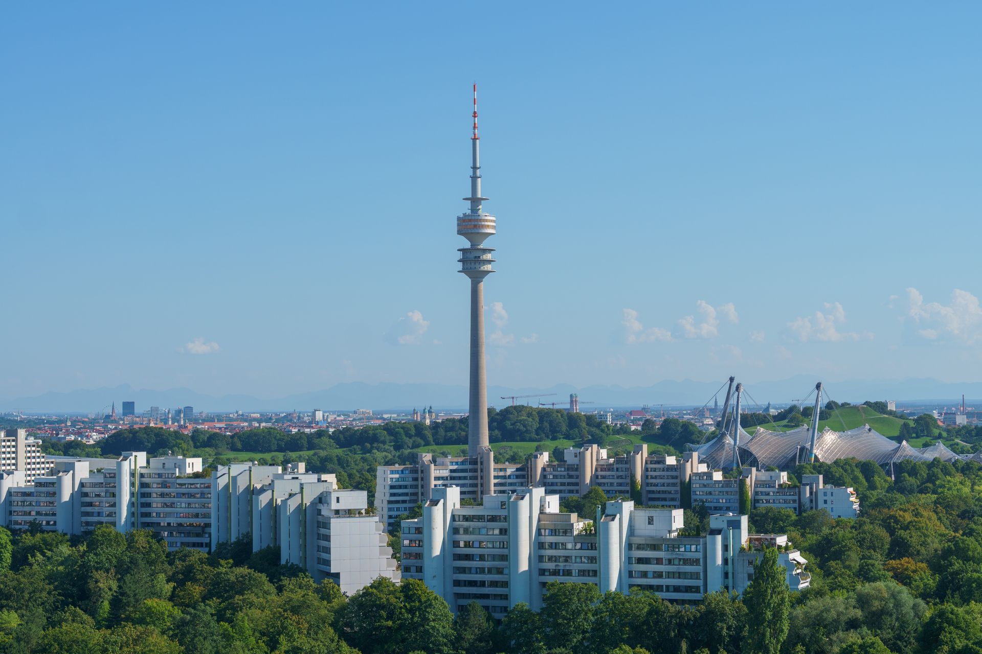 Aerial view of Munich featuring the iconic Olympic Tower and green landscapes in a clear blue sky.