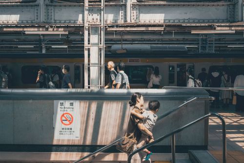 Free Commuters and a mother with child at a busy Tokyo train station, under sunlight. Stock Photo