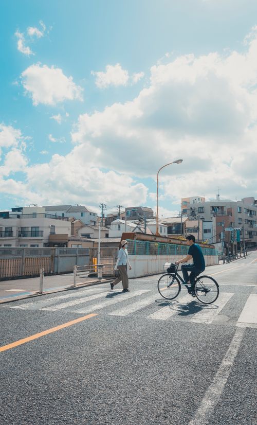 Free A bright day in Tokyo showcasing an urban street scene with a cyclist and pedestrian crossing. Stock Photo