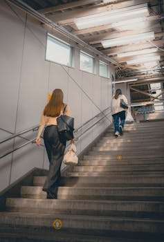 Two women walk up stairs in a modern Tokyo station, capturing urban life.