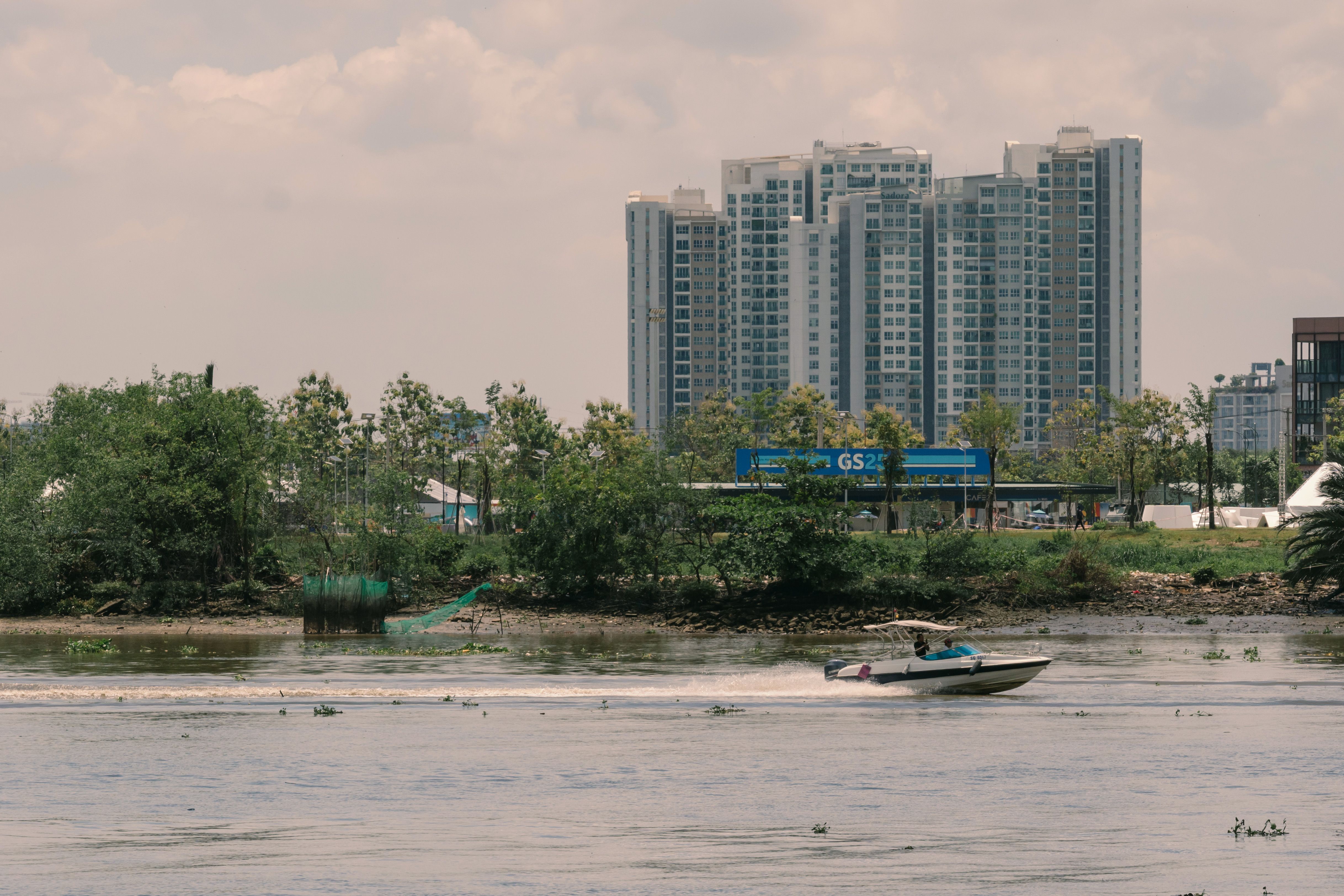 A speedboat travels swiftly across a river with modern city buildings in the background.