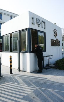 A security guard stands at a modern entrance booth during the daytime.