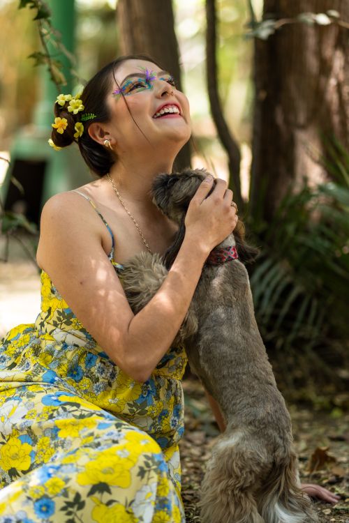 Free Joyful Latina woman with artistic floral makeup in park, embracing her dog, surrounded by nature. Stock Photo