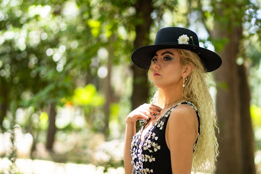 Elegant woman in black hat and floral dress posing in a sunlit park setting.