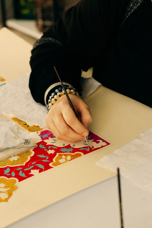 Free Close-up of artist painting a vibrant floral design on paper with brushes. Stock Photo