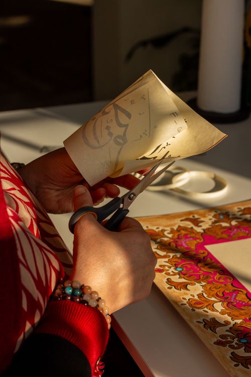 Free Person with scissors cutting patterned paper in artistic setting. Stock Photo