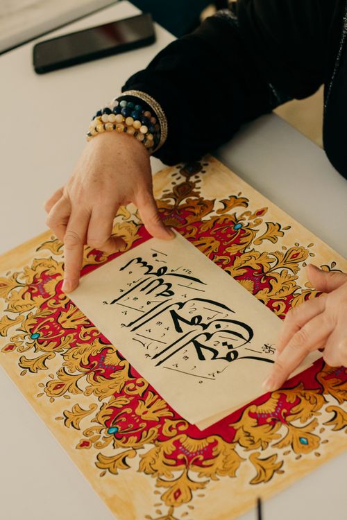 Free A detailed view of hands appreciating decorative Arabic calligraphy on ornate paper. Stock Photo