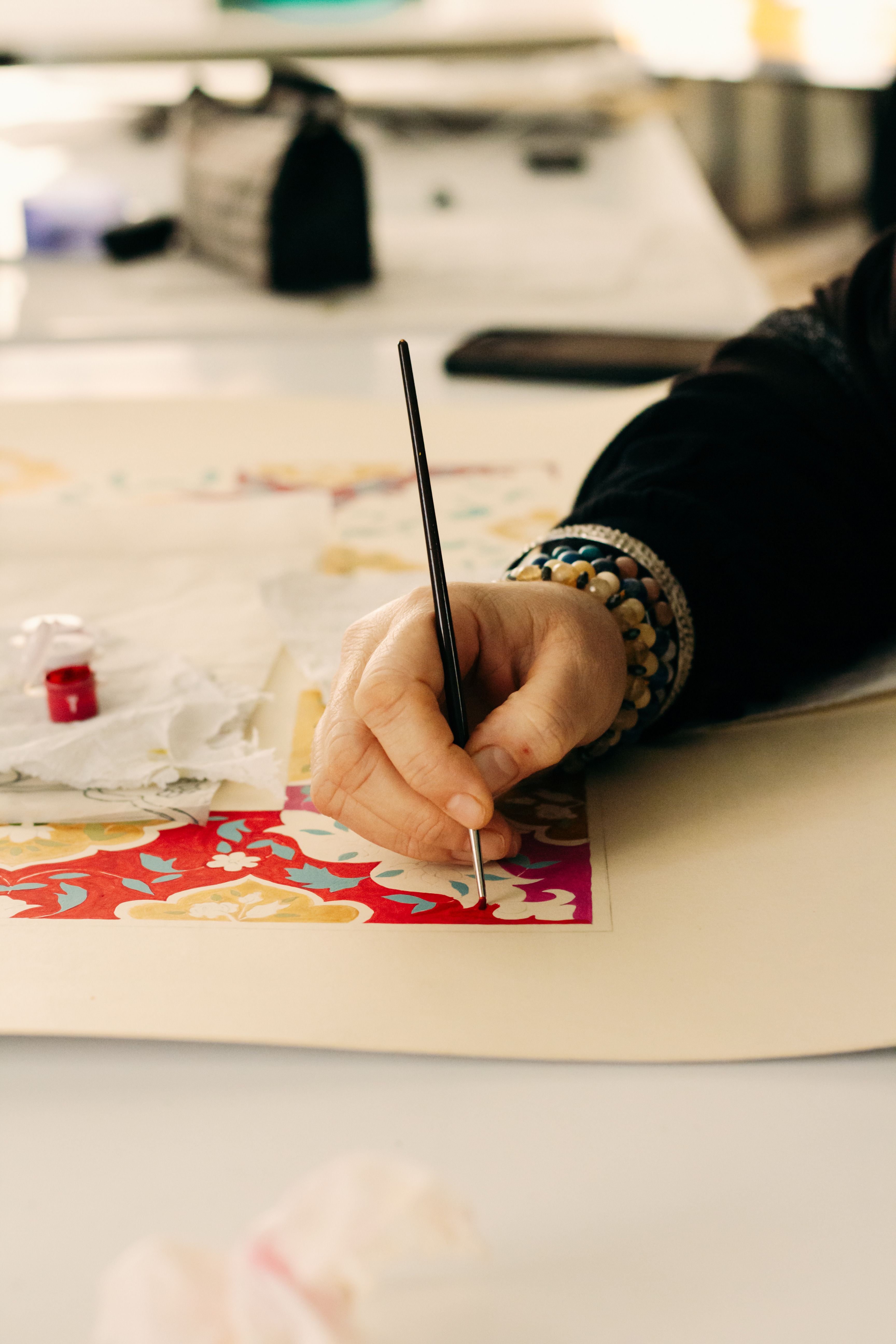 Close-up of artist's hand painting a vibrant floral pattern on canvas.