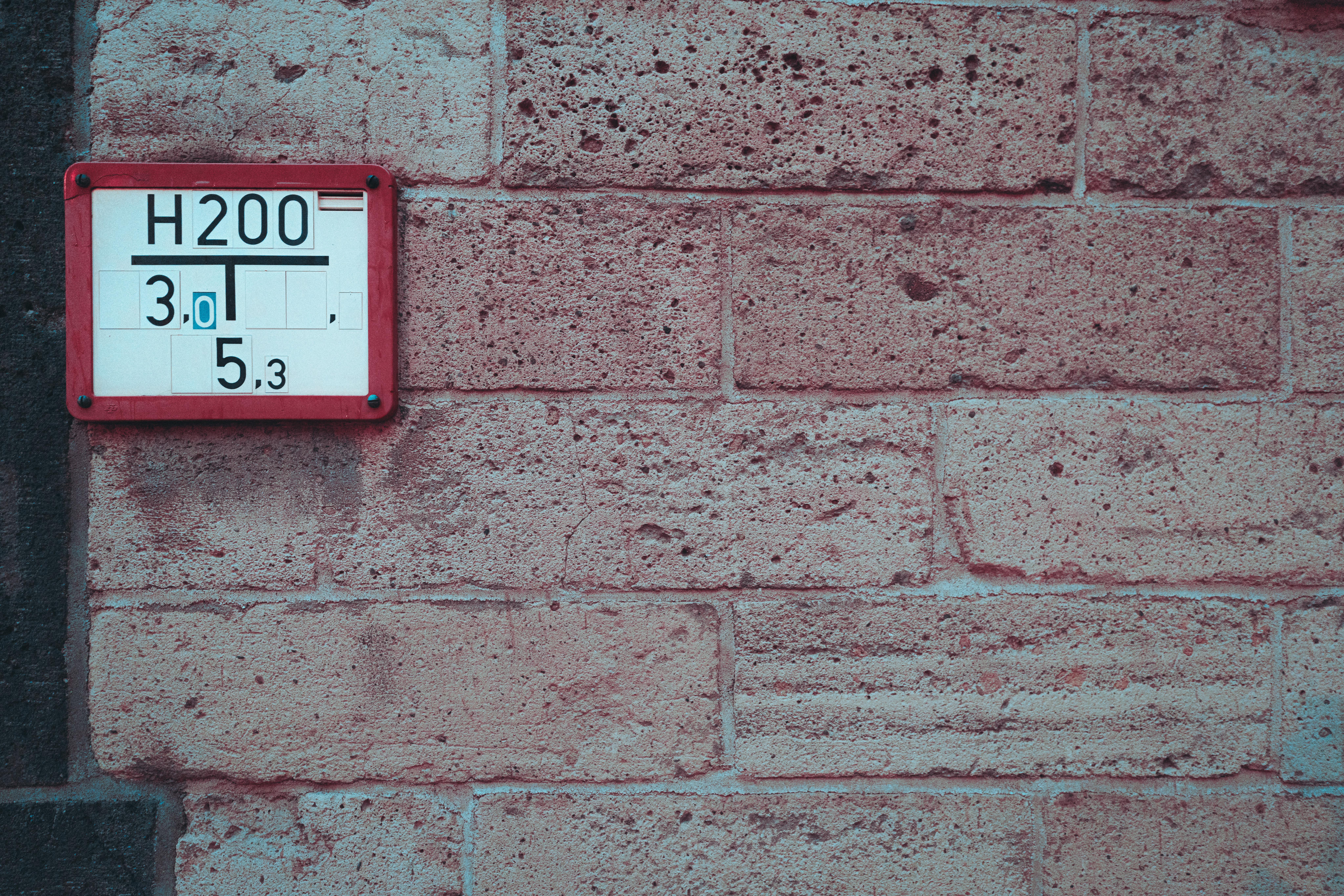 Gratis Primo piano di un muro di mattoni ruvidi su cui è posizionato un cartello di servizio con numeri, che offre un dettaglio urbano. Foto a disposizione