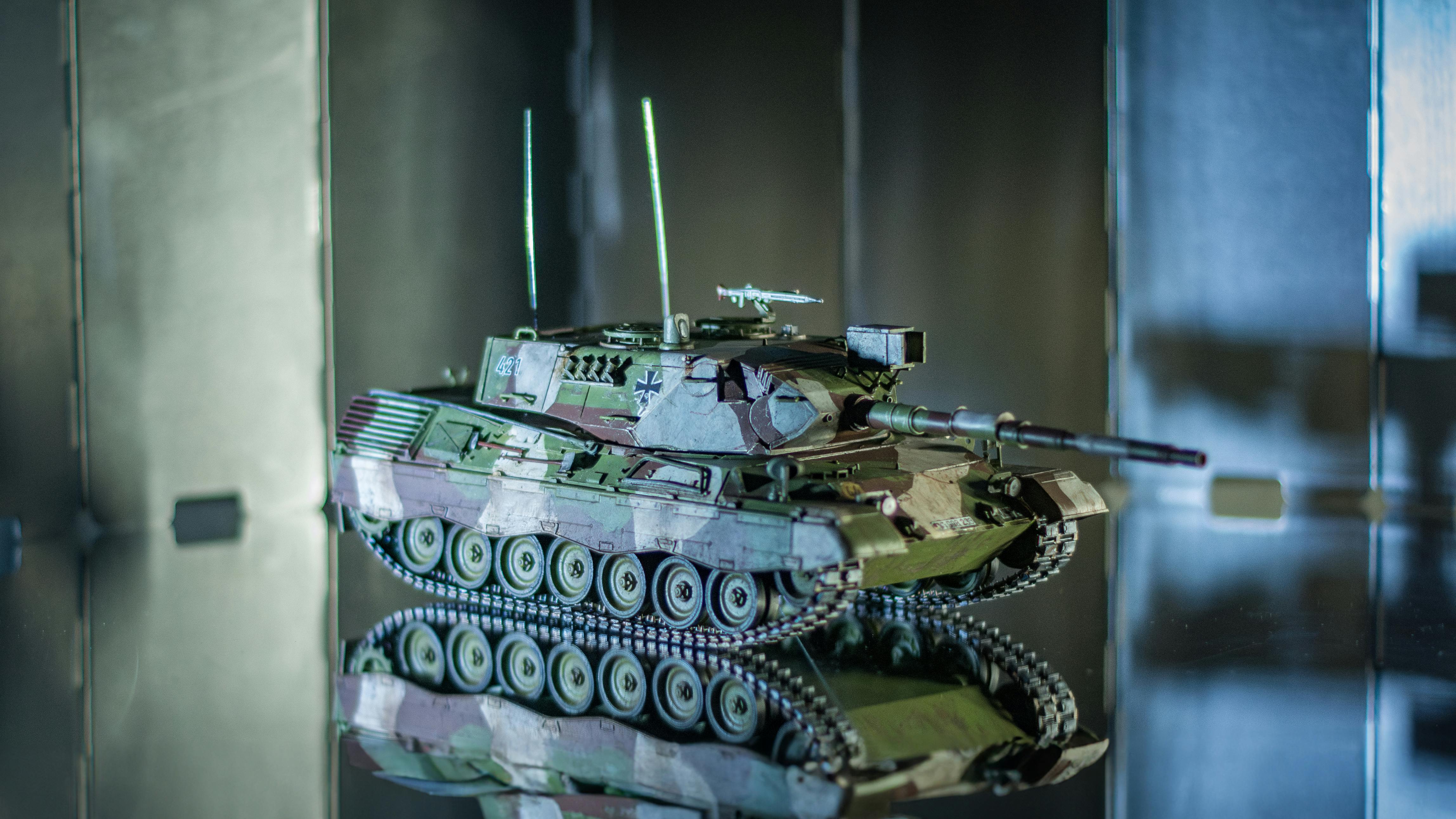 Gratis Nærbillede af en model tank med camouflage, der reflekterer på en overflade indendørs. Lagerfoto
