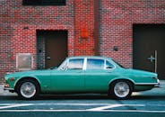 在城市环境中，一辆复古绿色捷豹汽车停靠在红砖墙边，凸显出经典汽车设计