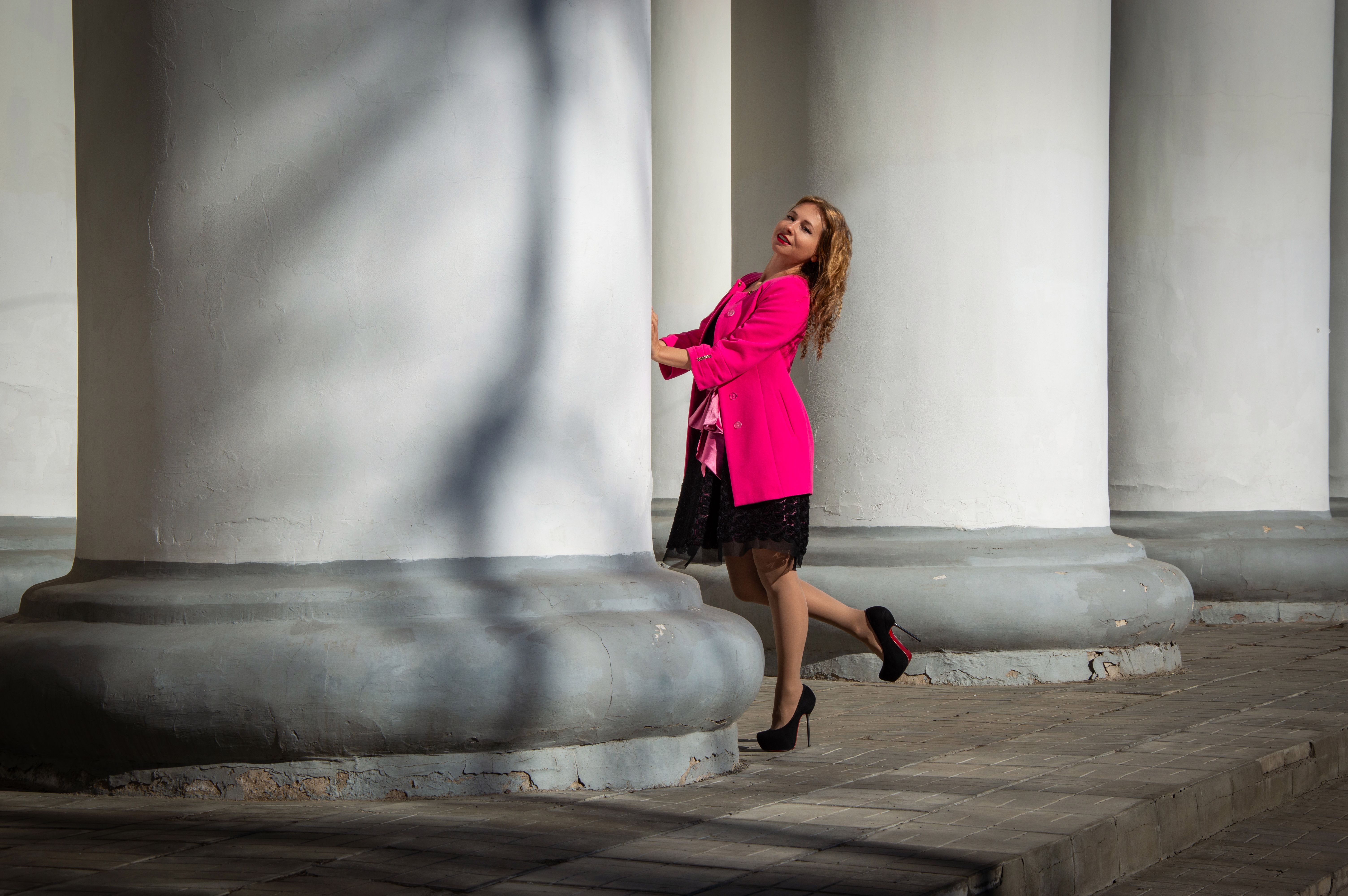 A woman in vibrant attire smiles while hugging a large column, showcasing modern style.