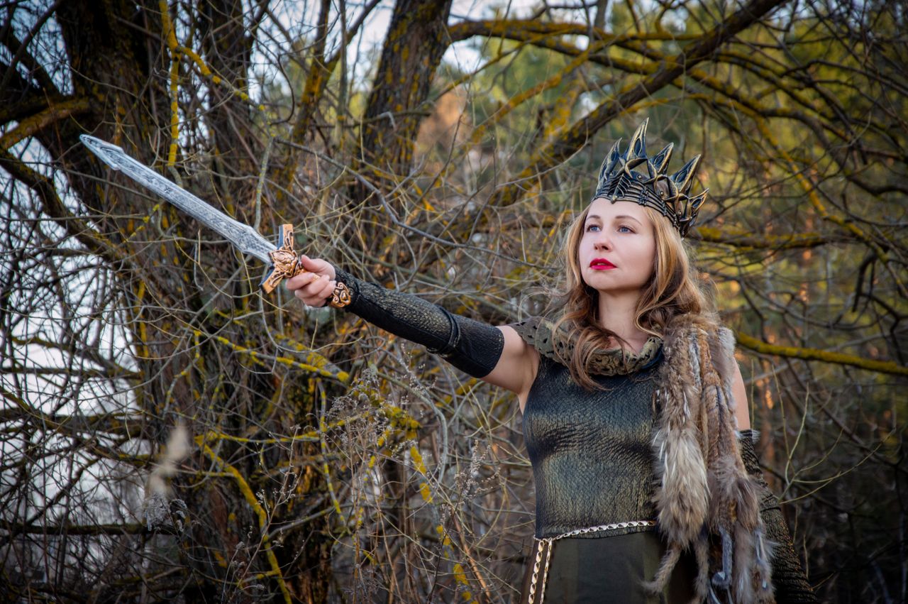a fierce warrior queen in medieval costume holding a sword against a f