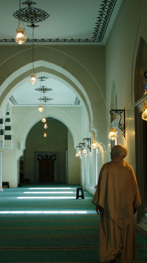 Free A person in traditional attire walks inside a mosque with beautiful arches and lighting. Stock Photo