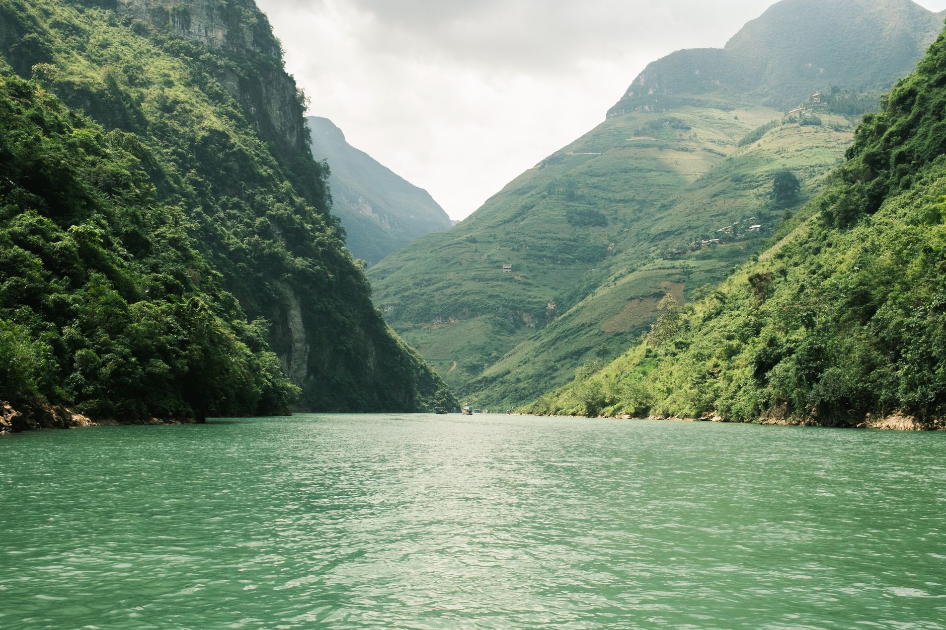 Serene view of a river flowing between lush green mountains under a cloudy sky.
