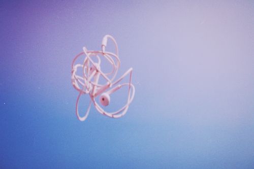 Free White earbuds suspended in mid-air against a pastel sky background, symbolizing technology and freedom. Stock Photo