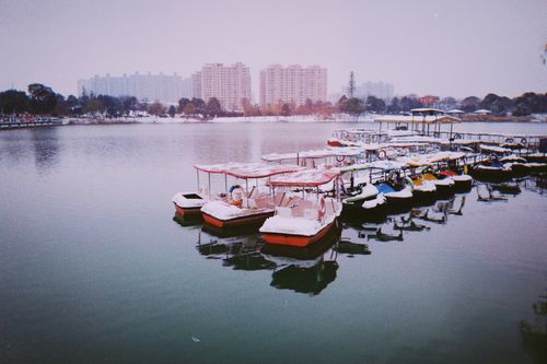 Free Snow-covered boats docked on a peaceful lake with cityscape backdrop in China during winter. Stock Photo