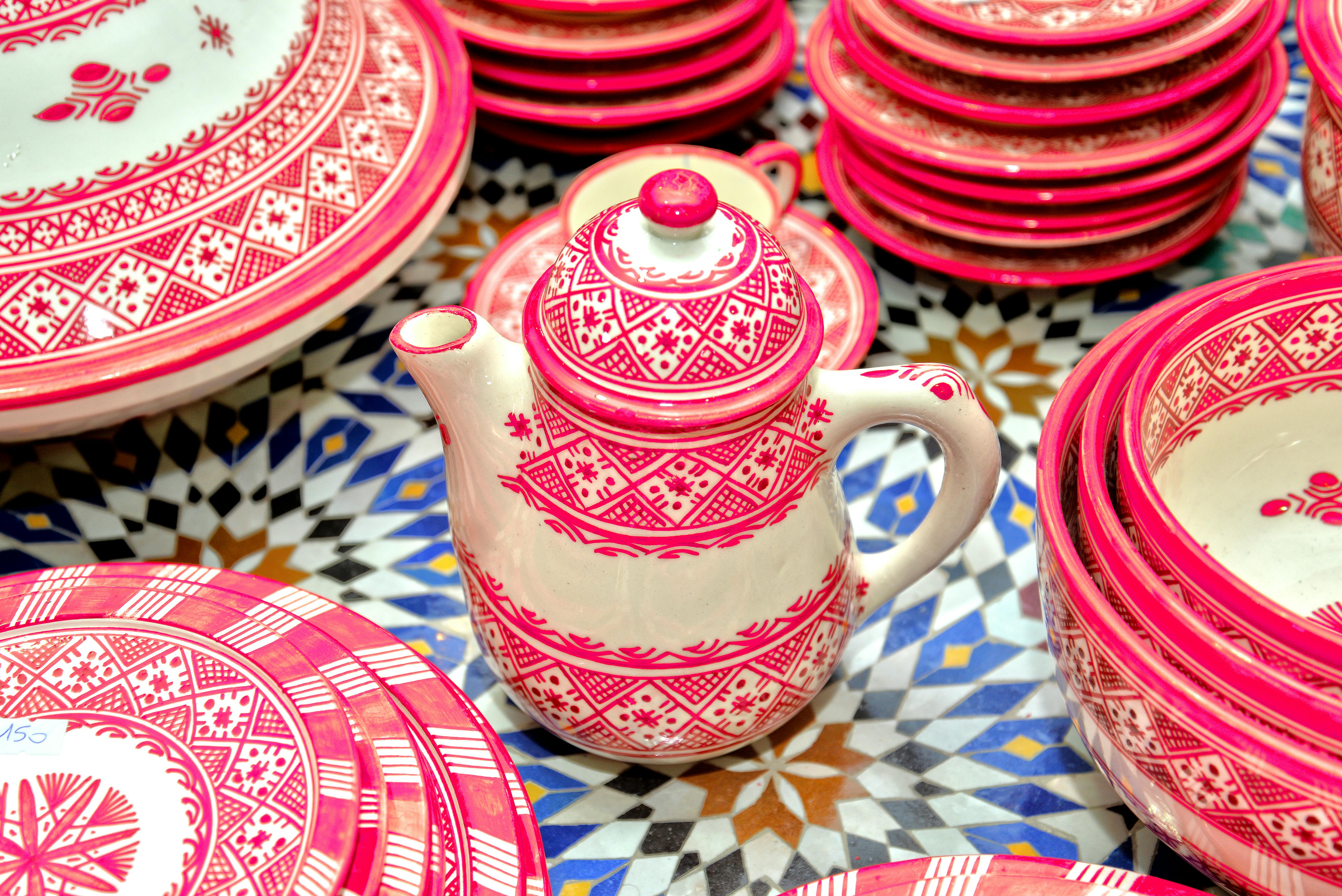 Handcrafted Moroccan pottery with intricate red designs displayed in Fès market.