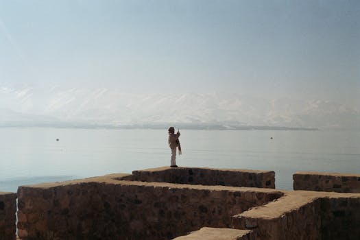 Serene winter view of a person by the lake in Van, Türkiye, with distant snowy hills.